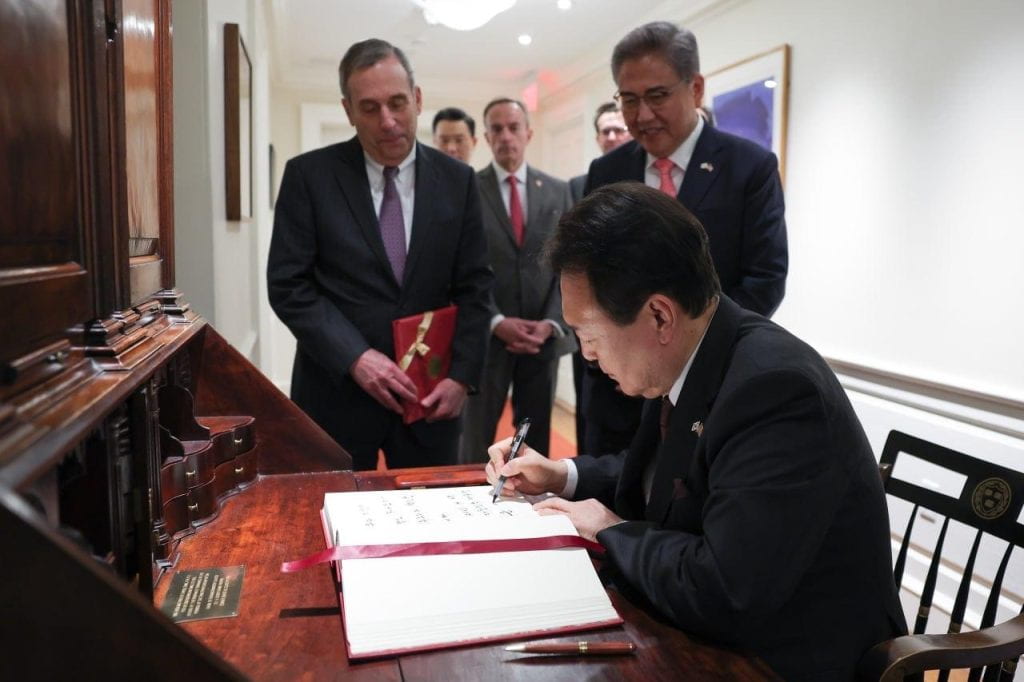 South Korean President Yoon Suk Yeol (front) signs the Harvard University Guest Book. behind him stands Harvard University President Larry Bacow (left), Vice Provost for International Affairs Mark Elliott (center), and Minister of Foreign Affairs of Korea Park Jin (right).
